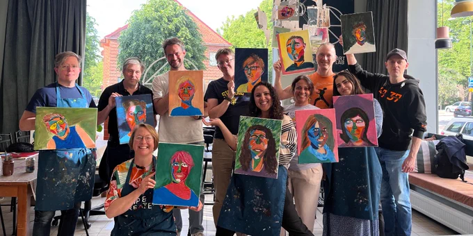 Members of the Øredev Program Committee in an art studio proudly displaying colorful abstract portraits they painted during a workshop.
