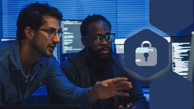 Two people wearing glasses collaborate at a workstation with multiple monitors displaying code, while a digital padlock icon overlays the scene to represent cybersecurity.