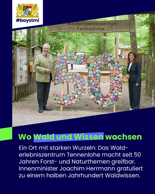 Zwei Personen stehen vor dem Walderlebniszentrum Tennenlohe neben einer bunten „50“-Skulptur zum 50-jährigen Jubiläum.