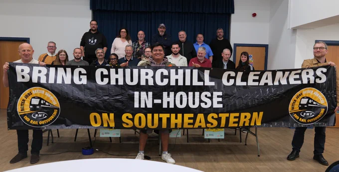 Group of people holding a large banner reading 'Bring Churchill Cleaners In-House on Southeastern' inside a community hall.
