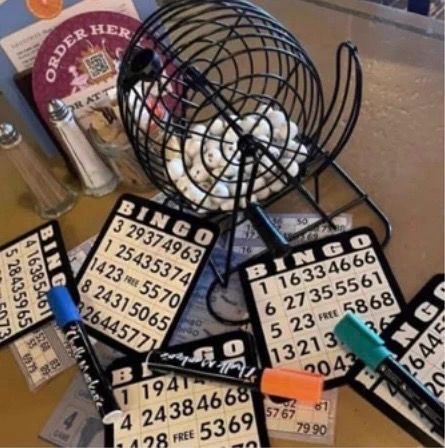 Photo shows a bing wheel, some bingo cards and some pens