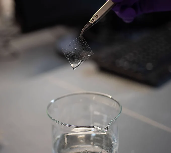 Ions of calcium and magnesium sticking to a membrane held up tongs over a beaker