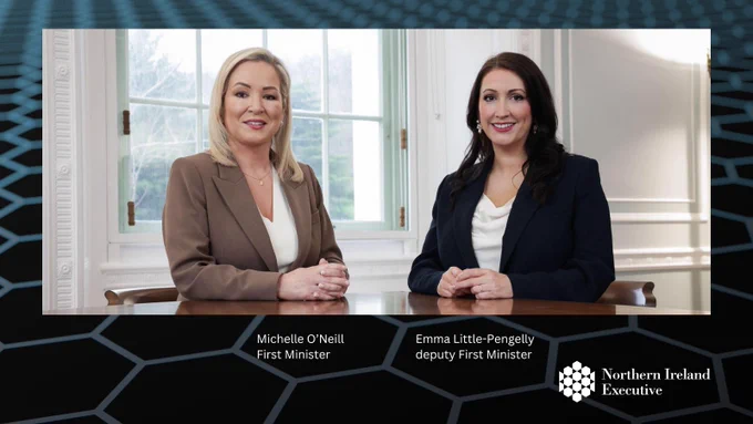Photo, Text, logo and arrow on hexagonal design background 
Photo: Image of two people - Michelle O’Neill First Minister, Emma Little-Pengelly deputy First Minister - sitting at table with window in background 
Text: Michelle O’Neill First Minister, Emma Little-Pengelly deputy First Minister  
Logo: Northern Ireland Executive logo at bottom centre of graphic 
Arrow: Arrow at bottom right of graphic