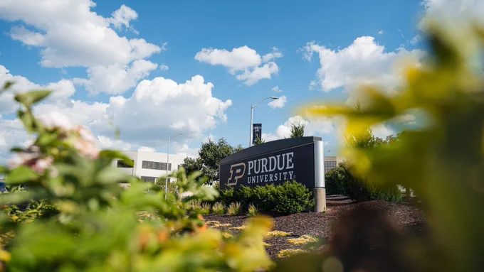 The Purdue University entrance sign surrounded by summer landscaping and blue skies at the Purdue Indianapolis campus.