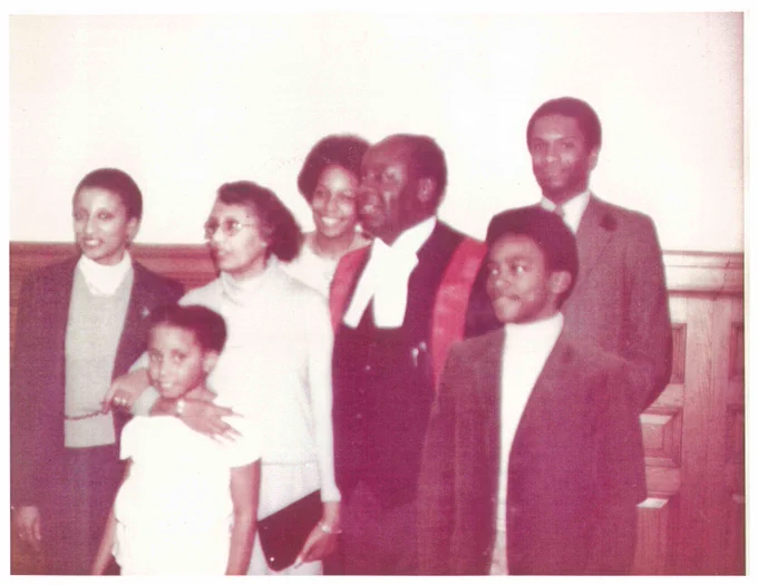 Group portrait of six people standing indoors, with one person dressed in formal judicial robes and others in casual attire.