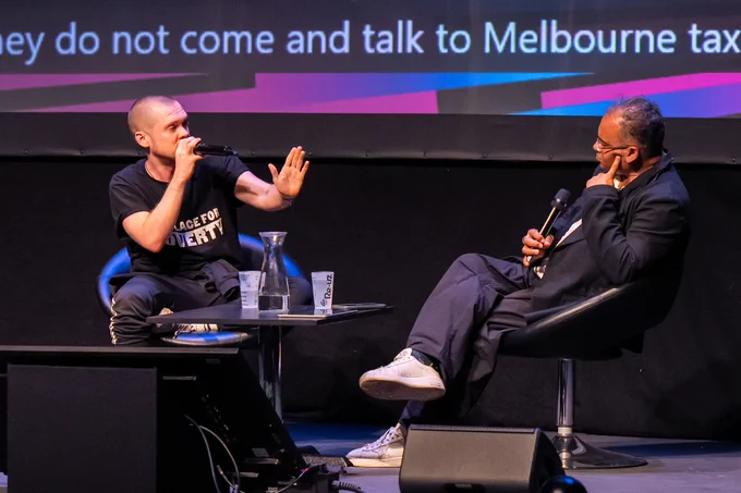 A close-up photo of two people sat onstage in conversation, each with microphones