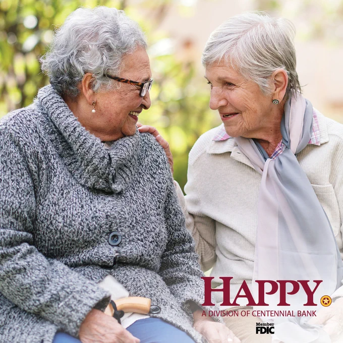 Two elderly women sitting outdoors, engaged in a warm conversation on a sunny day.