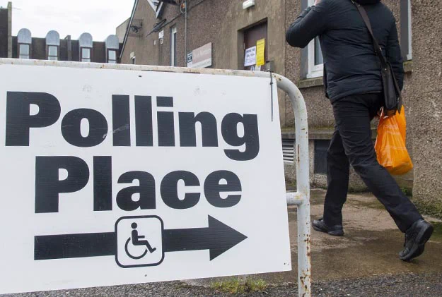 A sign indicates 'Polling Place' with an arrow and wheelchair symbol. A person walks away carrying an orange bag.