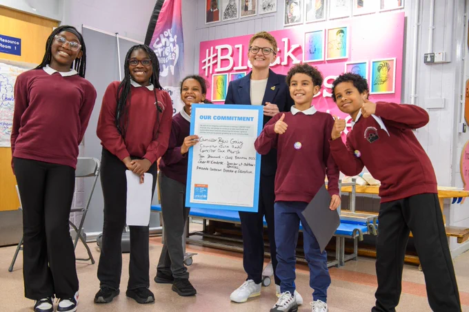 A group of schoolchildren and an adult hold a "Our Commitment" sign, with UNICEF branding, in a school setting.