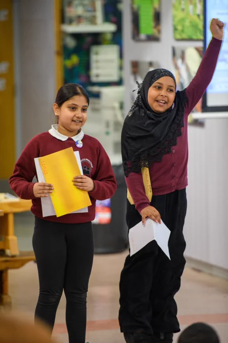 Two schoolgirls, one with her fist raised in triumph, participate in a school event.