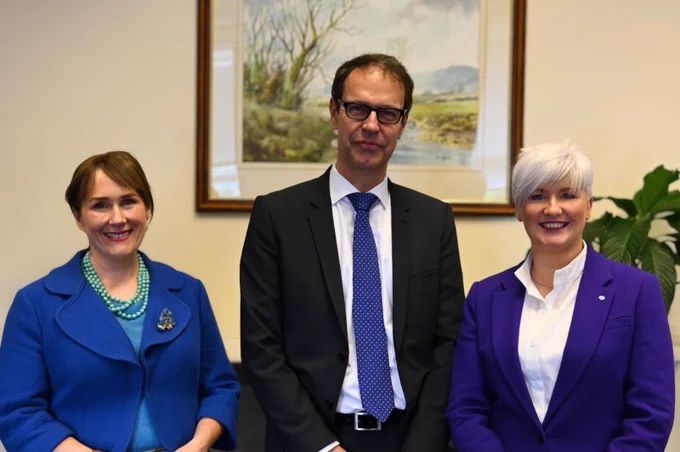 Picture of three people - including Junior Minister Joanne Bunting, Executive Office Permanent Secretary Moira Doherty and Ambassador of Switzerland to the UK, Dominique Paravicini - in front of a framed artwork.