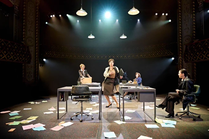 A photo showing a group of performers on a stage littered with paper