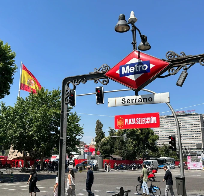 El acceso de la estación de Serrano, con el cartel indicador de Plaza Selección. Al fondo, la Plaza de Colón con la bandera de España.