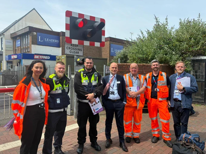 A group of people in a mix of PPE, security and office clothing are standing in front of a level crossing.