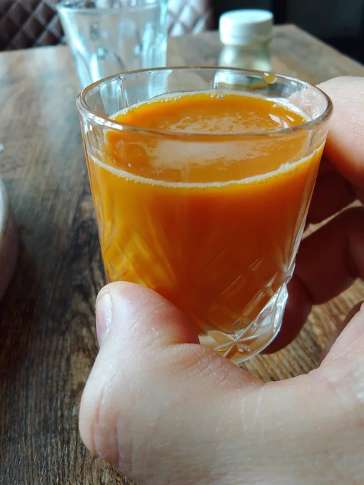 A Raw Juice Company shot of ginger, lemon, carrot, tumeric and black pepper in a glass.