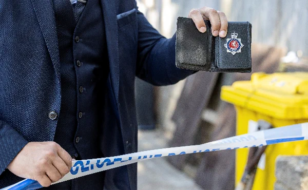 A police officer in a suit holding his warrant card up in front of a line of police tape.
