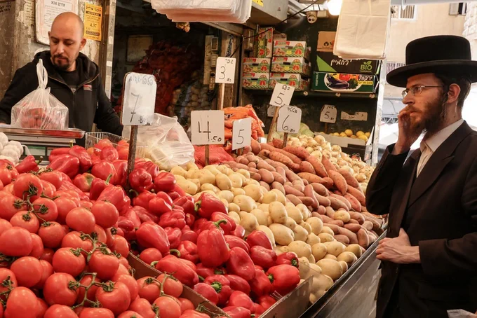 An ultra-Orthodox Jewish man stands in front of a vegetable vendor's stand at the Mahane Yehuda market before the start of Shabat, in Jerusalem on 31 January 2025 (Hazem Bader/AFP)