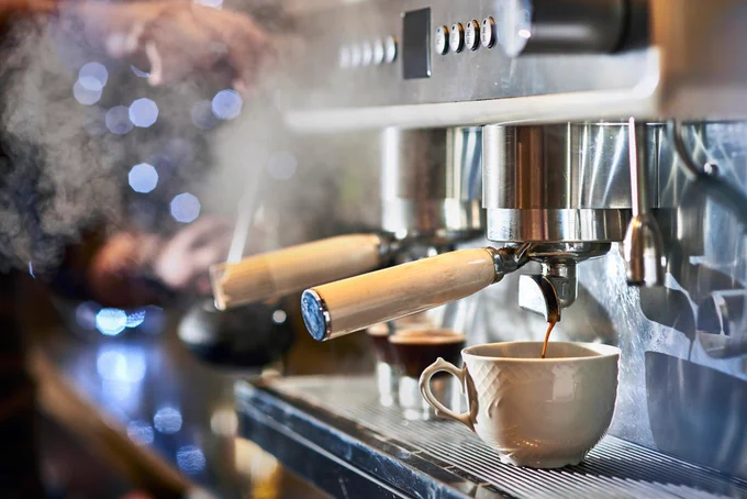 Espresso machine brewing fresh coffee into a ceramic cup with steam rising