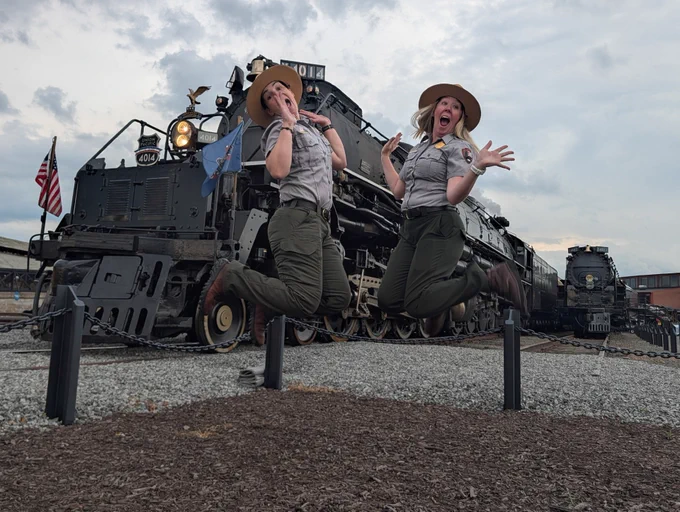 Two happy park rangers jump in front of Big Boy 4014 and 4012.
