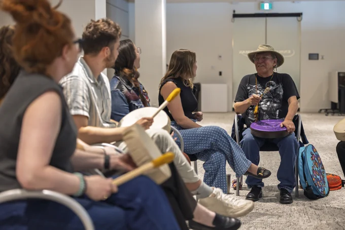Blackfoot Elder Sheldon First Rider explains Hand Games to a small group of people.