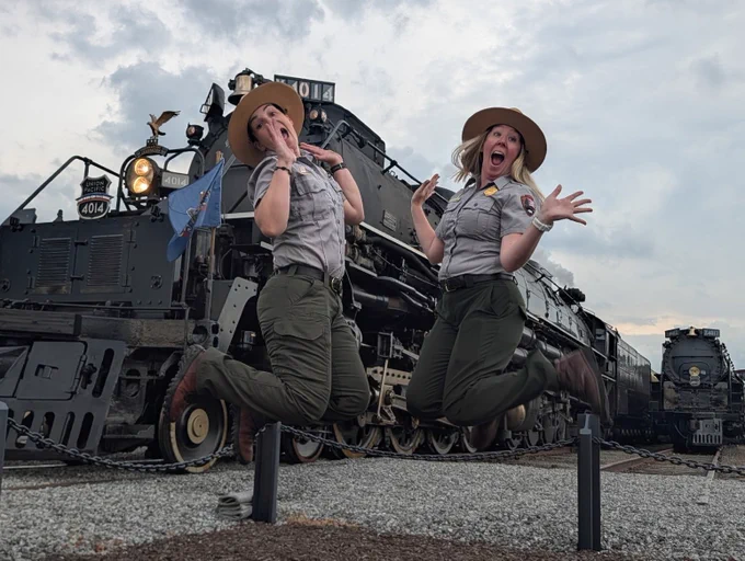 Two park rangers jump for joy in front of Big Boy 4014 and 4012 at Steamtown NHS.