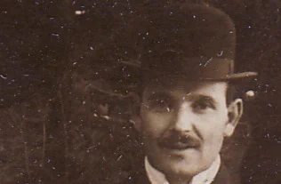 A man wearing a bowler hat with a slight smile in an old-fashioned.
