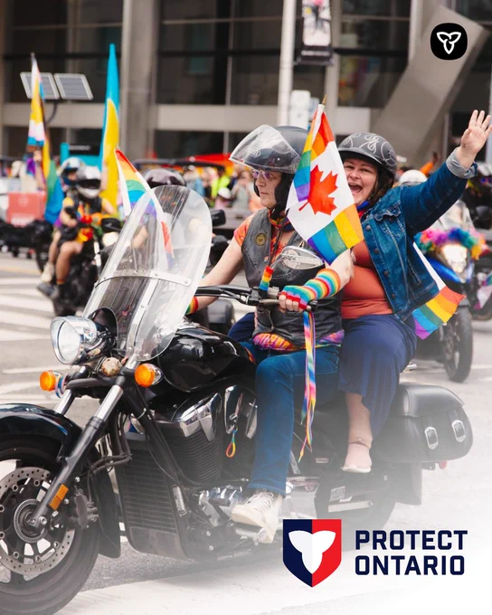 Two people ride a motorcycle in a Pride parade, holding rainbow and Canadian flags, while others on motorcycles follow behind. The Protect Ontario logo appears in the corner.
