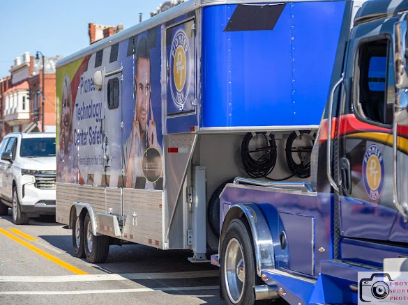 Blue mobile technology center truck parked on a city street with promotional graphics on its side.