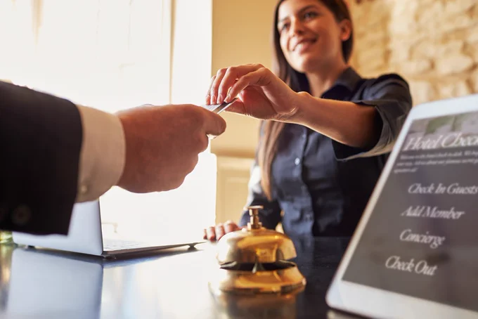Hotel receptionist handing a key card to a guest across the front desk with a service bell nearby.