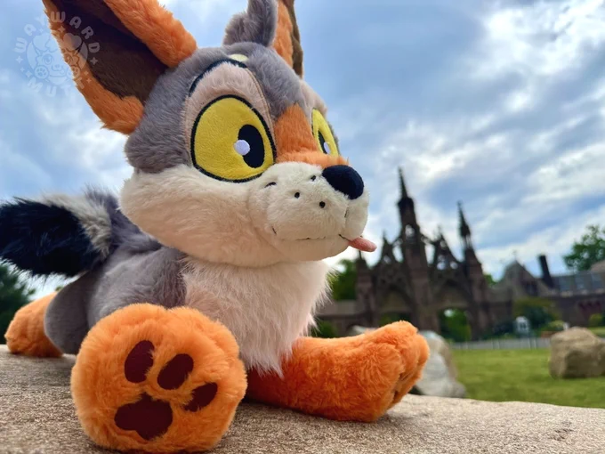 Yote plush lounging on a rock with a blue sky behind him.