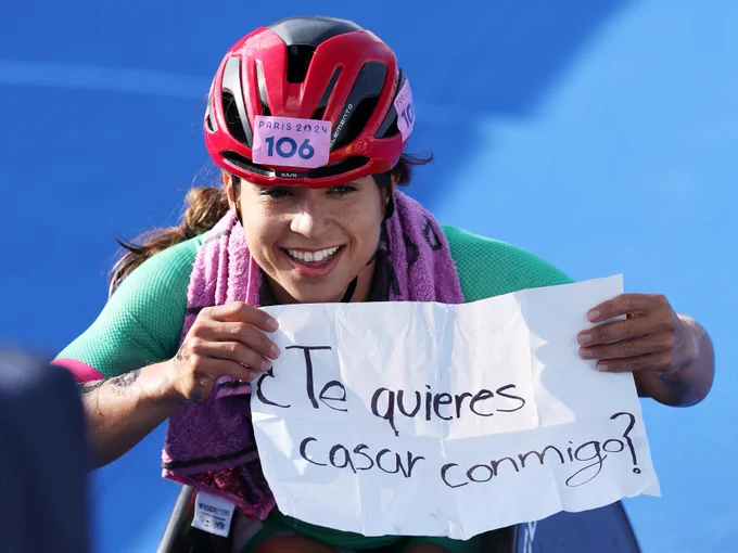 Brenda Osnaya proposing to her girlfriend on the triathlon finish line at Paris 2024. She is holding a sign that reads: Te quieres casar conmigo