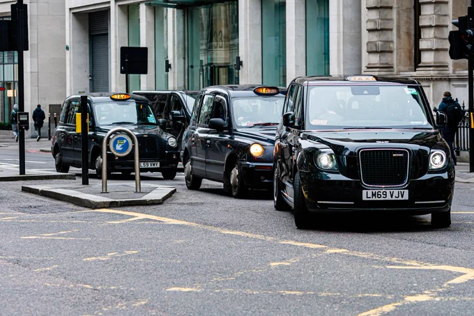 Three black taxis queued on a city street at an intersection.