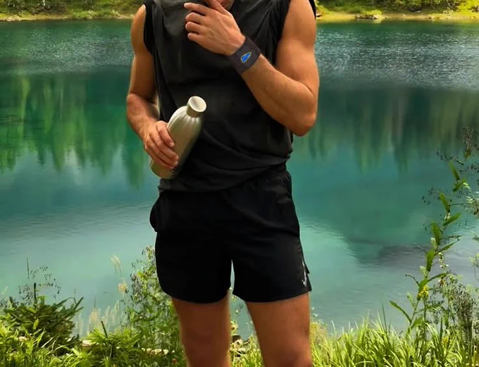 Man in running shorts and tank top in front of a body of water in the woods 