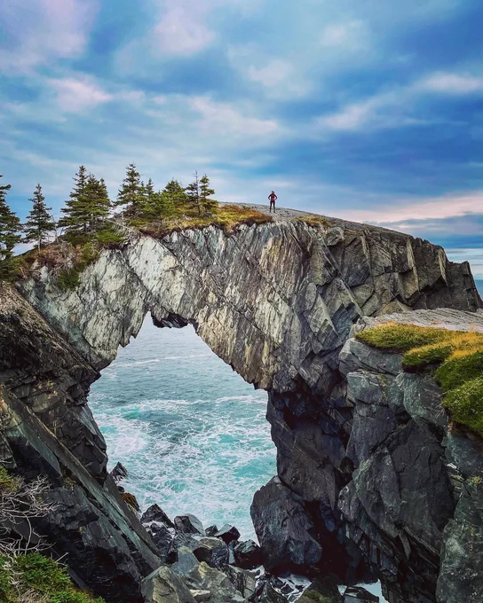 The Berry Head Sea Arch in Newfoundland and Labrador, with a blue ocean and cloud-filled sky in the background. 