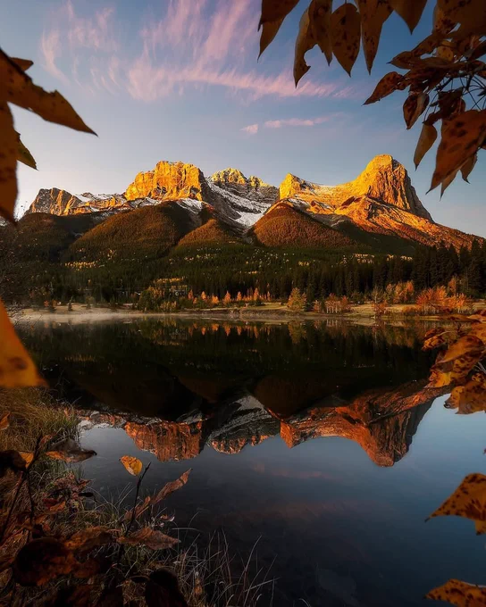 A scenic lake sits in the foreground of the image, with a fall-foliage covered mountain behind it. 