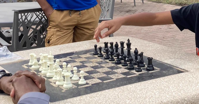 Two people play chess as a third stands nearby.