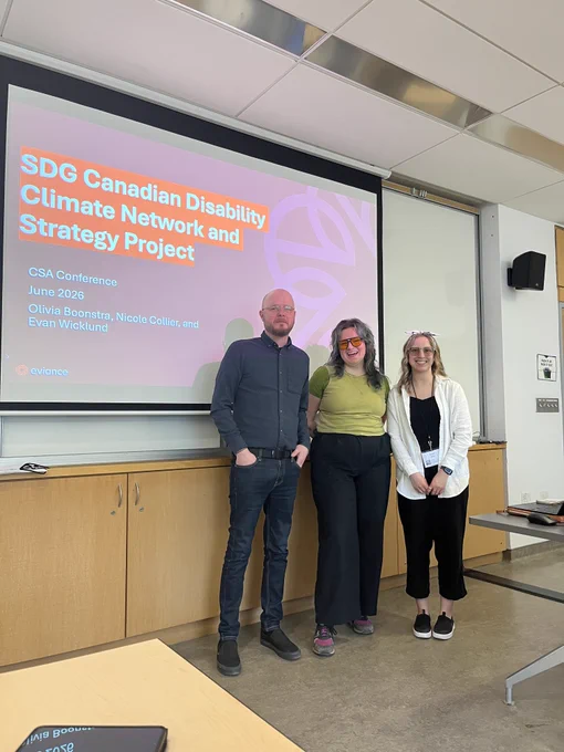 Three team members from Eviance—Evan, Olivia, and Nicole (from left to right)—stand together in a classroom presentation space. Behind them, a large projector screen displays a pink slide titled "SDG Canadian Disability Climate Network and Strategy Project" for the CSA Conference in June 2026.