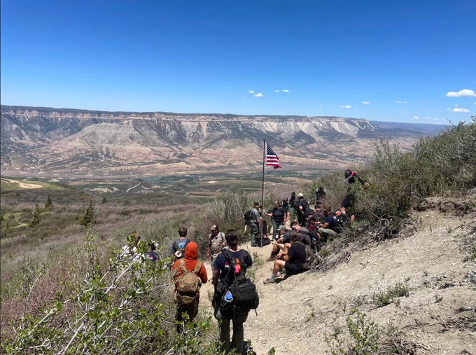 Group of fire employees resting on a hillside with an American flag overlooking a vast canyon under a clear blue sky.