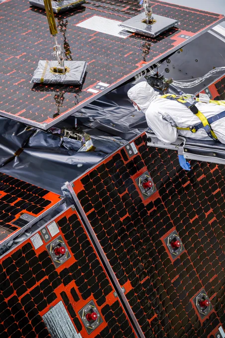 A technician wearing white clean room protective attire installing Nancy Grace Roman Space Telescope's solar array Sun shield — a set of solar panels on the telescope. The panels are dark with red outlines. Credit: NASA