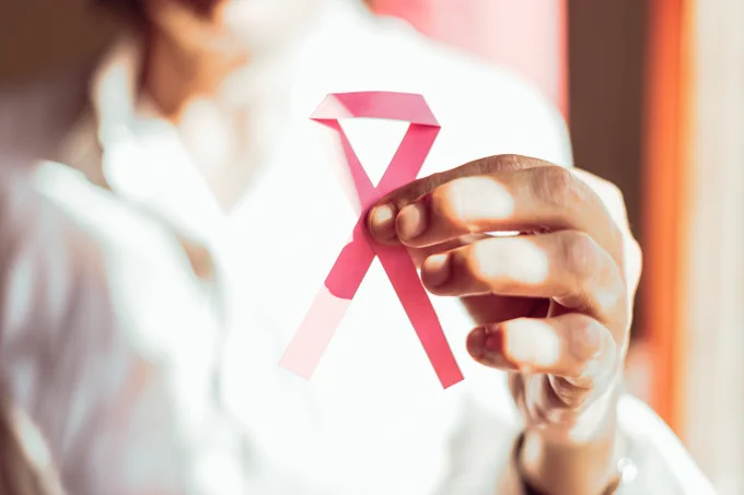 A person holding a pink ribbon, symbolizing breast cancer awareness.