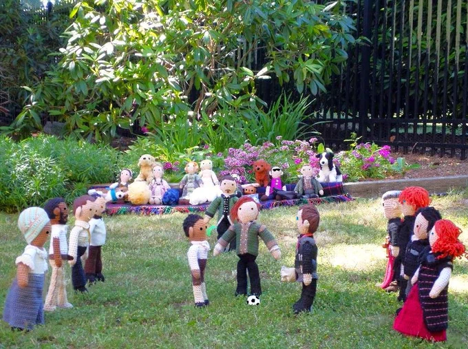 Crochet dolls l-r in foreground: Abigail, Akinbode, Marshal Kahler, Caleb Brewster, Cicero, William Guppy with Nicholas Farlow beyond him, Karl Tanner, Don Bruciare Gormangia, John Graves Simcoe, Ross & Demelza Poldark all standing ready for the kick off. More crochet fans & toy dogs in background with garden.