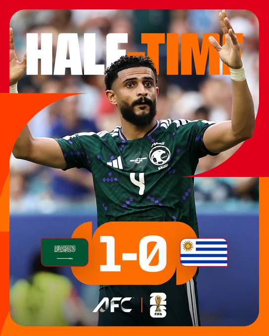 A Saudi Arabian football player celebrates during halftime with Saudi Arabia leading Uruguay 1-0. The graphic prominently shows the halftime score, alongside the flags of both teams.