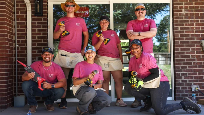 A group of six people in matching Blitz Build t-shirts holding power tools.