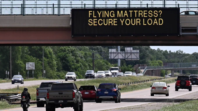 Electronic sign on highway above traffic. The sign reads, "Flying mattress? Secure your load.’”