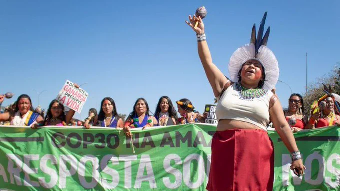 Mulheres indígenas marcham na rua segurando faixa verde escrita COP30 na Amazônia - A Resposta Somos Nós.