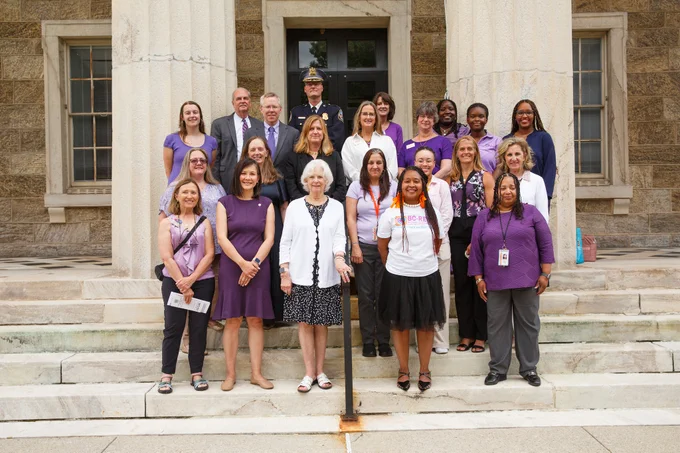 Photo of attendees posing together at the press conference. They are at the steps of the Historic Courthouse in Towson and wearing shades of purple.