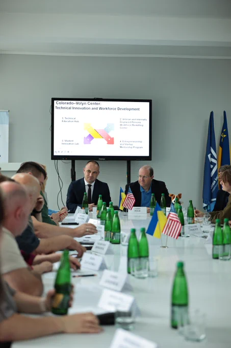 Conference room meeting with delegates discussing technical innovation and workforce development, featuring American and Ukrainian flags on the table.