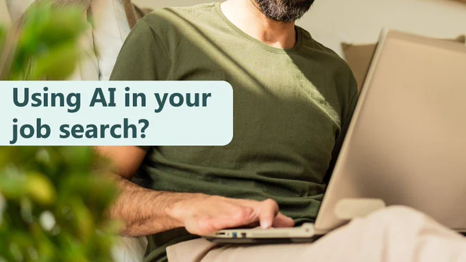 A person sitting indoors using a laptop on their lap. The person is wearing a green T‑shirt and light trousers, and only the torso and hands are visible. Sunlight falls across the scene, and a blurred green plant is in the foreground. A text box on the left reads: “Using AI in your job search?”