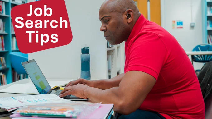 Person in a red top sits at a desk in a library or study space, typing on a laptop. Bookshelves and chairs are visible in the background, with a water bottle and study materials on the desk. A red graphic panel in the top corner reads “Job Search Tips” in bold white text.