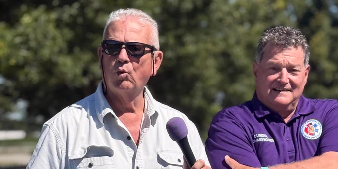 two men standing on a pickleball court and one is holding a microphone